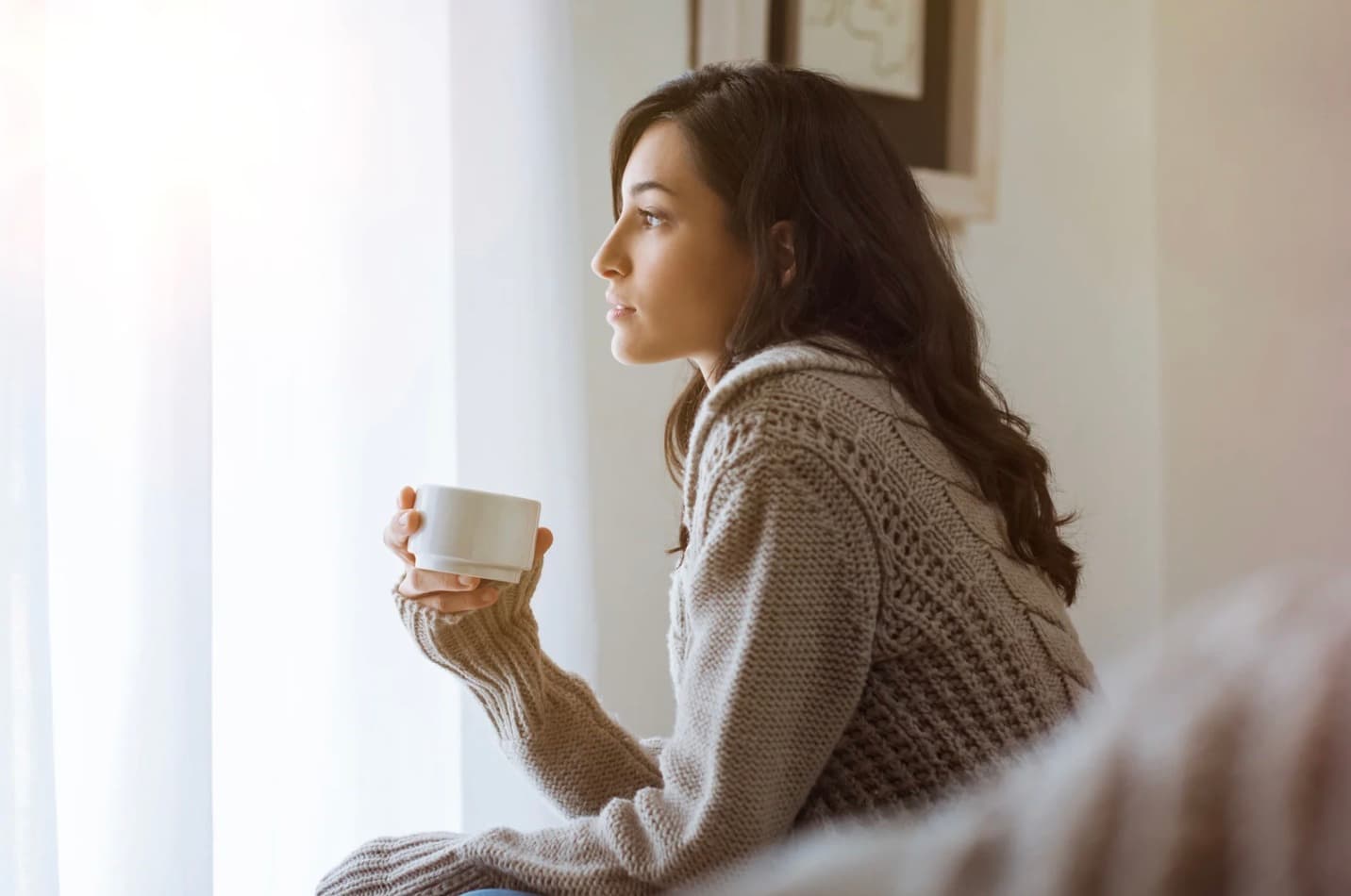 Illustrative photo of a woman holding a mug beside a window